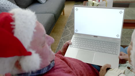 senior caucasian couple in santa hats with laptop with copy space at christmas, slow motion