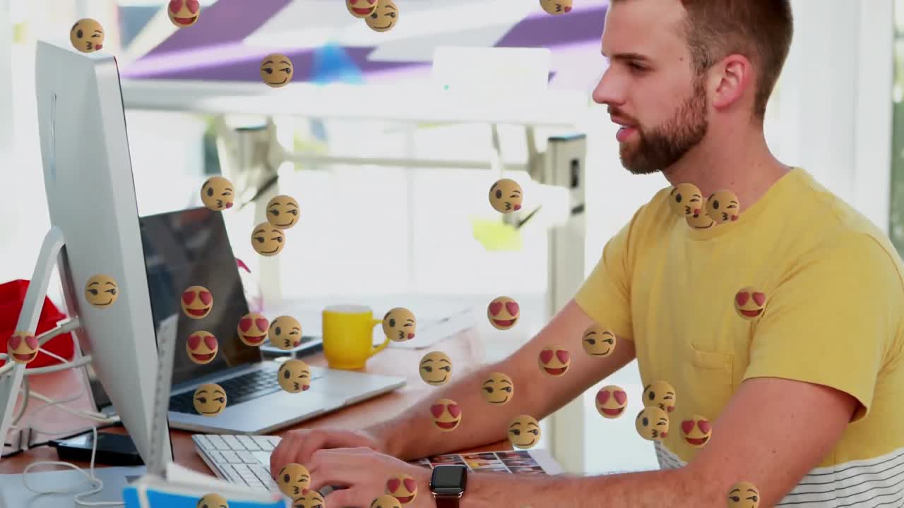 múltiples emojis de cara flotando contra el hombre usando la computadora en la oficina