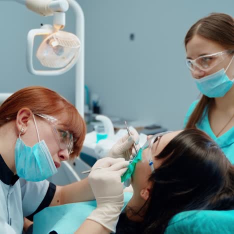 stomatologist treats tooth with medical tools. female dentist together with a nurse treating woman's teeth in clinic. stomatology concept.