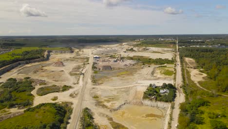 flying above vast open pit quarry mining site of limestone materials extraction, overburden piles and dust roads. exposed rock layers, surface mining for construction industry under cloudy summer sky