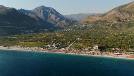 a scenic coastline with boats and people near a green sea and mountains in the distance, aerial view