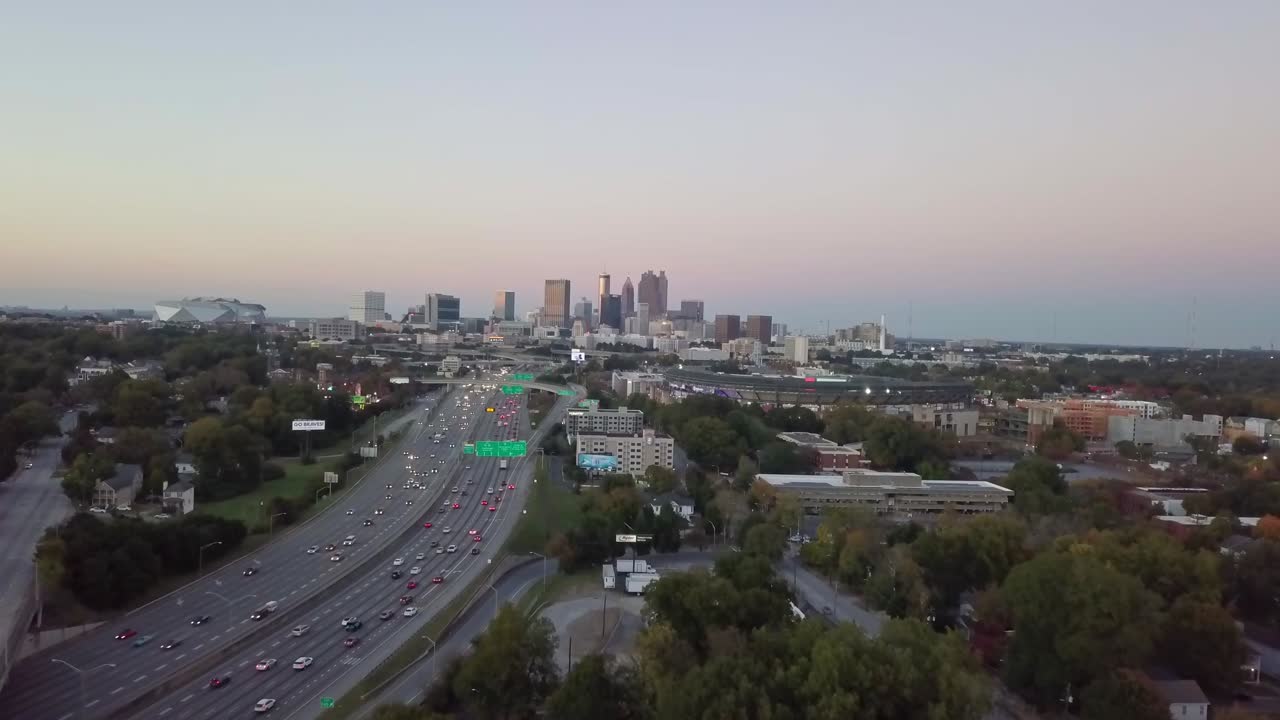 Ariel drone shot over skyline buildings in Atlanta, USA. Pretty tall skyline over busy highway road with cars driving through.  Tall Buildings and beautiful evening sunset view.