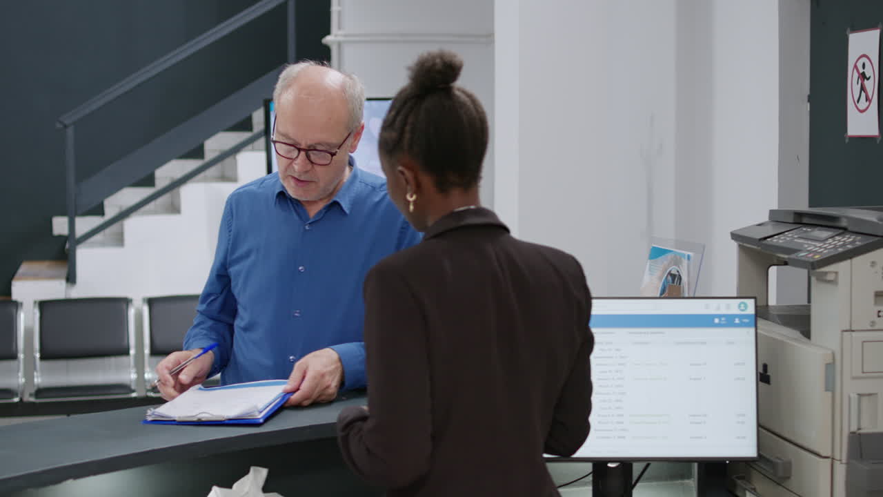 Patient signing medical form at hospital reception with receptionist