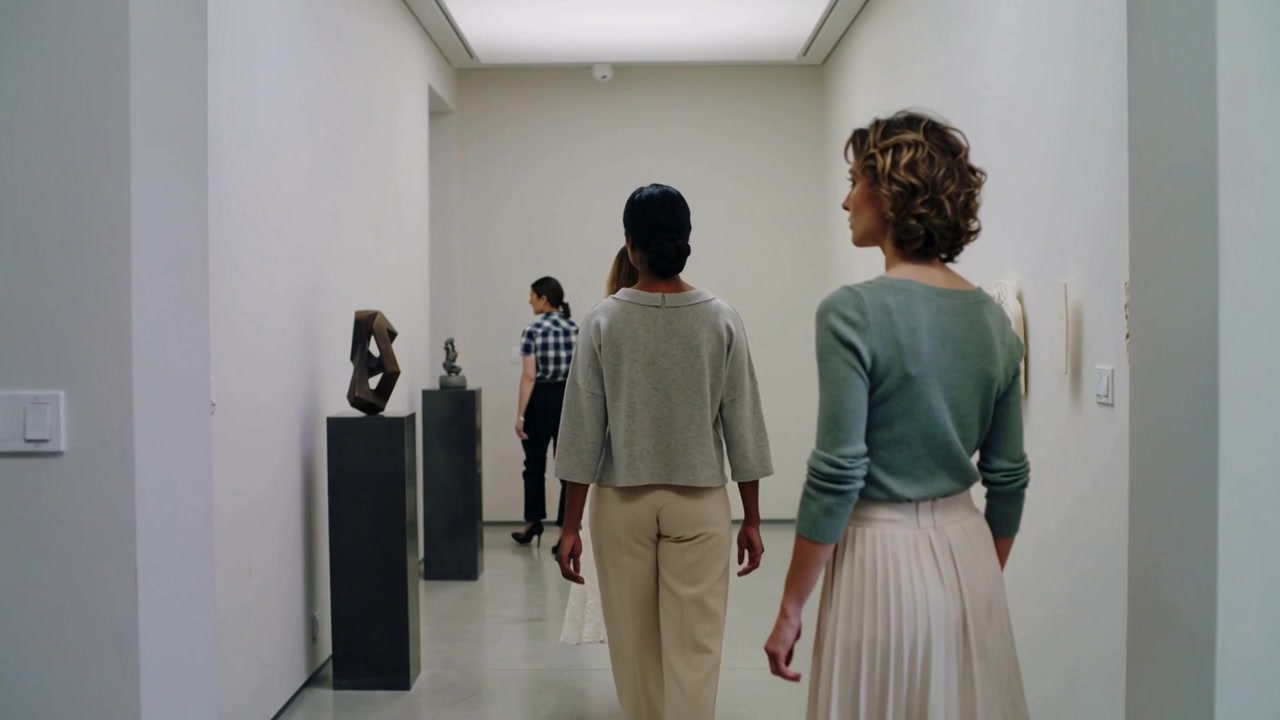 Tre donne in abiti eleganti camminano, entrando in una galleria e percorrendo un corridoio del museo.