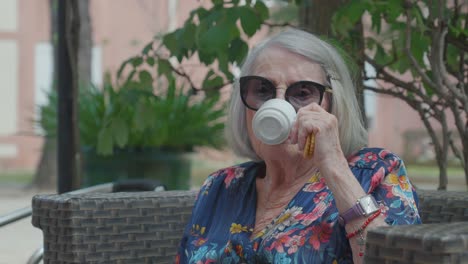 lovely older woman with sunglasses sips her tea with a cookie in her hand on a sunny day