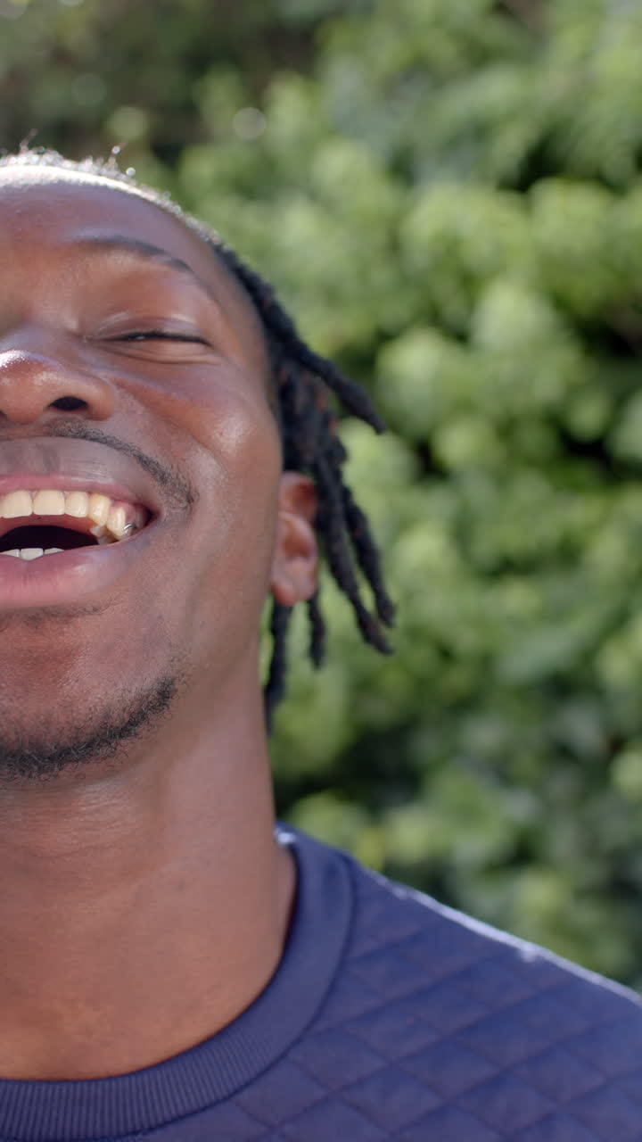 Vertical video of half portrait of happy african american man in sunny garden, slow motion