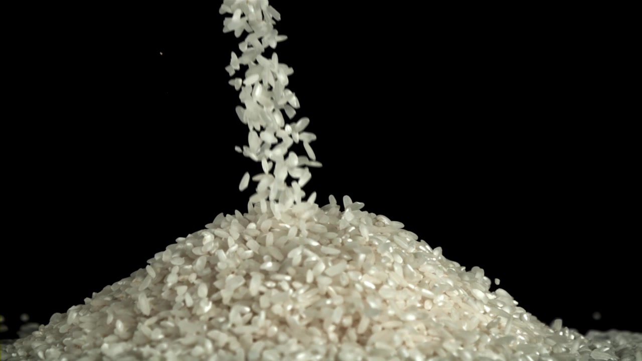Chicchi di riso bianco che cadono e si accumulano su sfondo nero