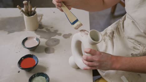 mid section of female potter wearing apron using glaze brush to paint on pot at pottery studio