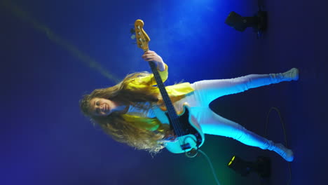 vertical video of a cheerful energetic female guitarist dancing and jumping in the light of strobe lights and spotlights