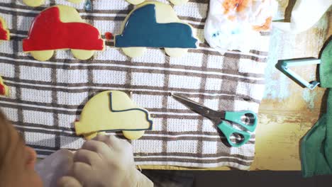 woman decorates homemade vehicle shaped cookies with sugar icing, overhead pan view 4k