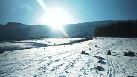 Panorámica-A-Través-De-La-Montaña-Inglesa-Cubierta-De-Nieve-Con-Destello-De-Lente-Natural-Del-Sol-De-Invierno