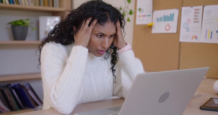 African American woman getting voicemail speaking into phone opening laptop and doing work at desk