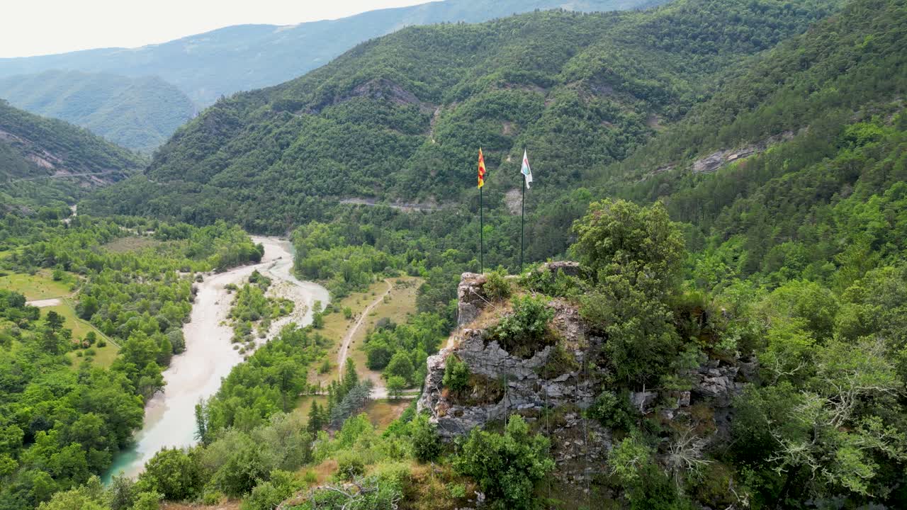 Drone footage of waving Flags infront of a peaceful french village in the hills, with vibrant summer landscapes all around.