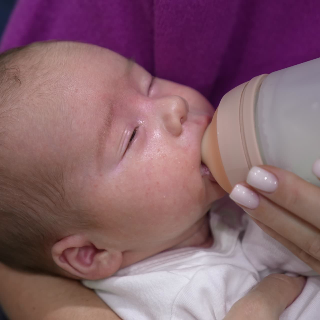 Toddler eating milk from bottle and closing sleepy eyes. Baby gradually falling asleep while eating. Close up