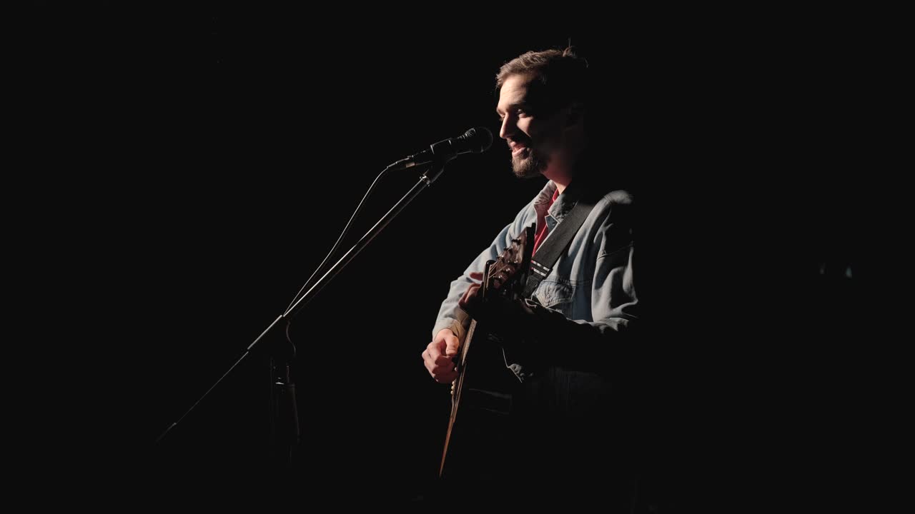 A musician is playing guitar on a large stage with audience members holding flashlights in the background. The auditorium is filled with beautiful flashing lights.