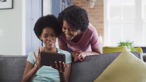 Happy-african-american-mother-and-daughter-sitting-on-sofa-using-tablet