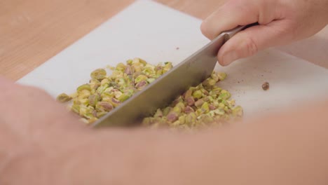 close-up of hands chopping pistachios on a cutting board, in slow motion