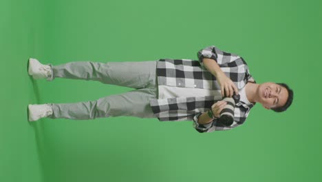 full body of asian photographer using a camera taking pictures and smiling while standing on green screen background in the studio