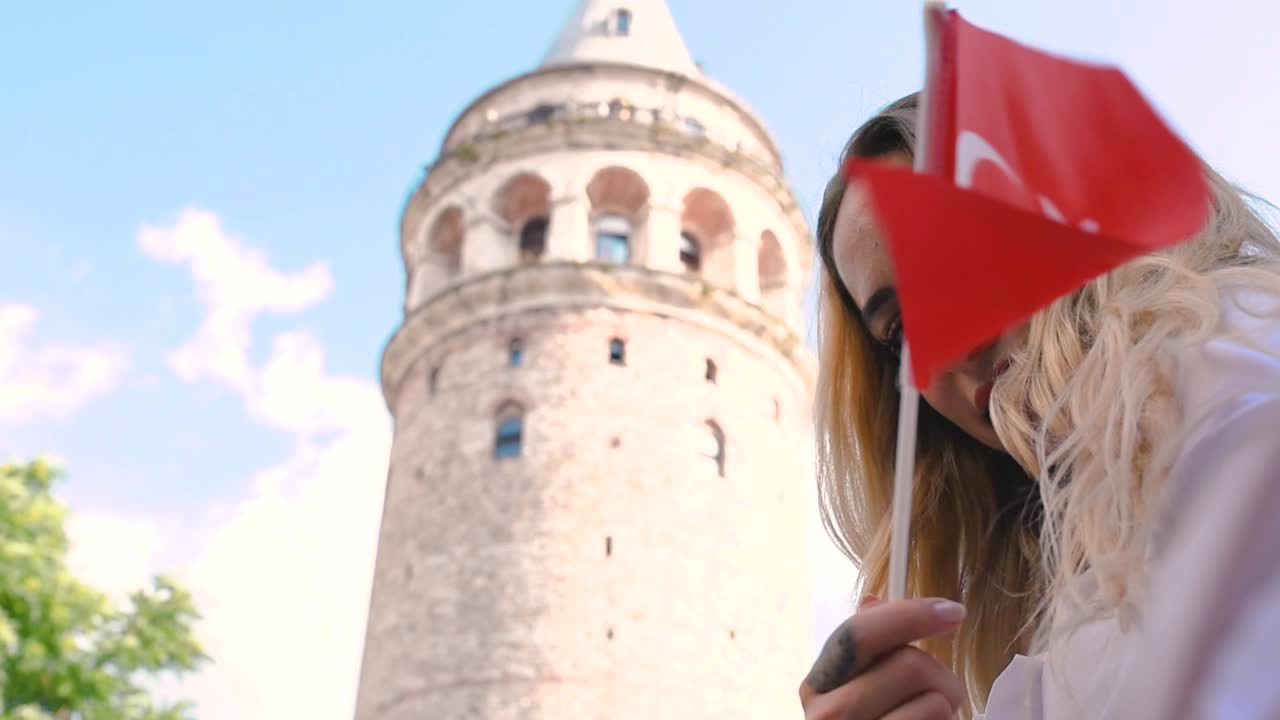 cámara lenta: atractiva joven hermosa toma selfie y ondea la bandera turca frente a la torre de galata, un punto de referencia popular en estambul, turquía