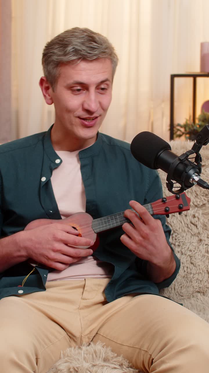 Young man joyfully plays toy ukulele recording fun music and singing in microphone with creativity