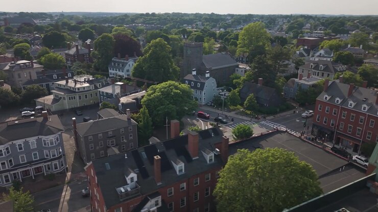 La Casa delle Streghe di Salem domina l'angolo della strada a Salem, Massachusetts; la torre di una chiesa in pietra si erge sopra una strada alberata e le auto parcheggiate sotto. Ripresa aerea con drone.