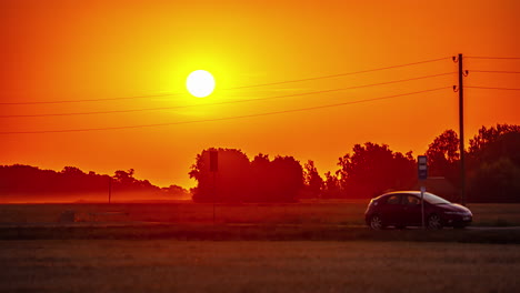 timelapse shot of the rising sun along red sky over trees in an open rural landscape during morning time