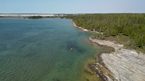 Vista-Aérea-Del-Piragüismo-Familiar-A-Lo-Largo-De-La-Costa-Del-Surco-Del-Glaciar,-Desierto-De-Bush-Bay,-Islas-Les-Cheneaux,-Michigan