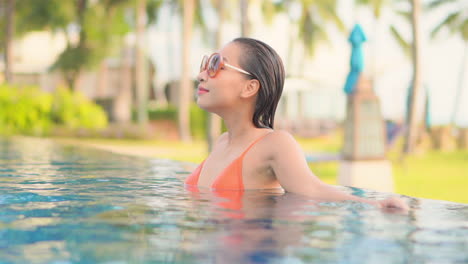 woman wearing large sunglasses relaxing in infinity swimming pool of beautiful luxury tropical resort