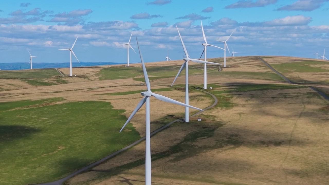 Large Wind Farm with Long Straight Road and Dramatic Blue Sky. Aerial Drone Clip of Renewable Energy Generation Infrastructure in UK. 4K.