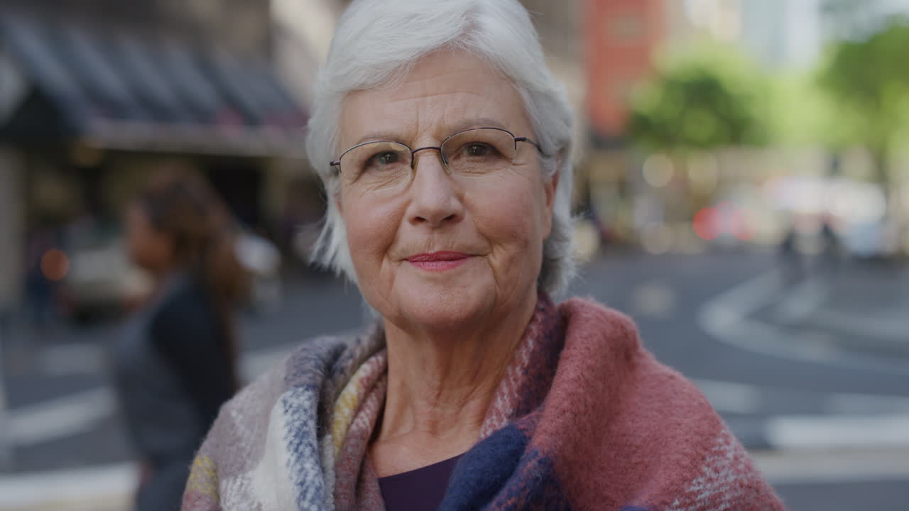 retrato de uma mulher idosa confiante sorrindo olhando para a câmera usando um lenço na rua da cidade de fundo em câmera lenta
