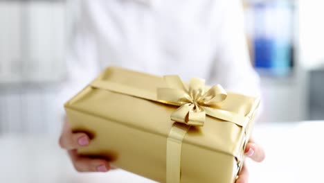 person gives gift in box with golden packaging and bow