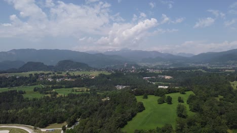 Toma-Panorámica-Ascendente-Que-Muestra-El-Paisaje-Verde-Del-Distrito-De-Bled-Y-La-Cordillera-En-El-Fondo---Eslovenia,-Europa---Toma-Amplia-De-Drones