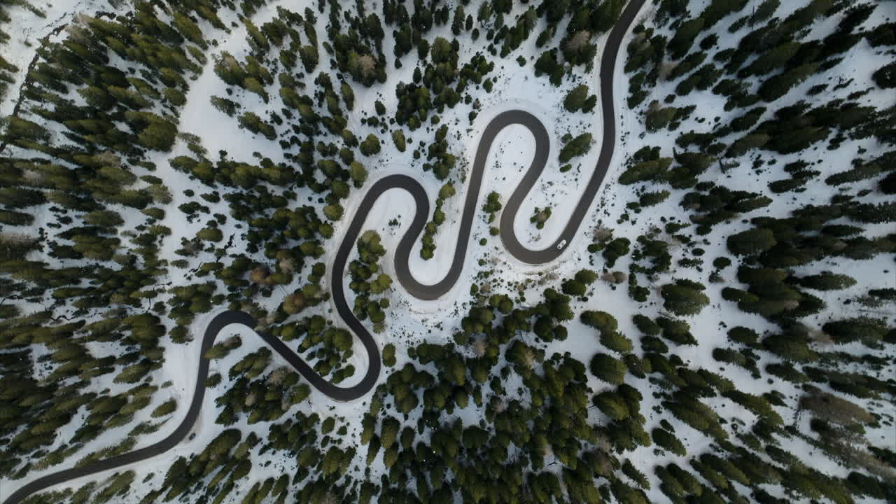 toma rotativa aérea de arriba hacia abajo de una sinuosa carretera de montaña entre el bosque de coníferas cubierto de nieve en los dolomitas