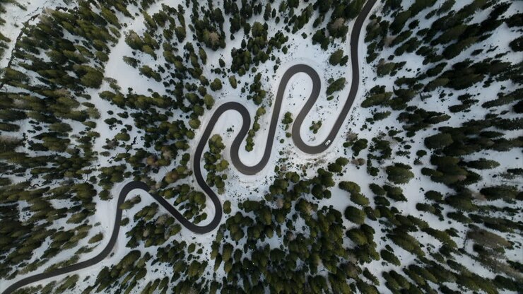 Aerial top-down rotating shot of winding mountain road between snow-covered coniferous forest in the Dolomites