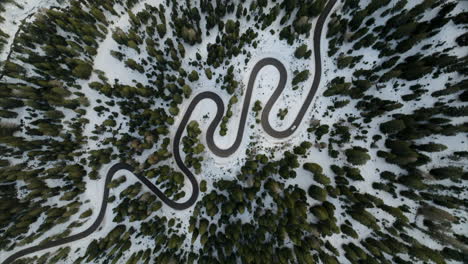 Aerial-top-down-rotating-shot-of-winding-mountain-road-between-snow-covered-coniferous-forest-in-the-Dolomites