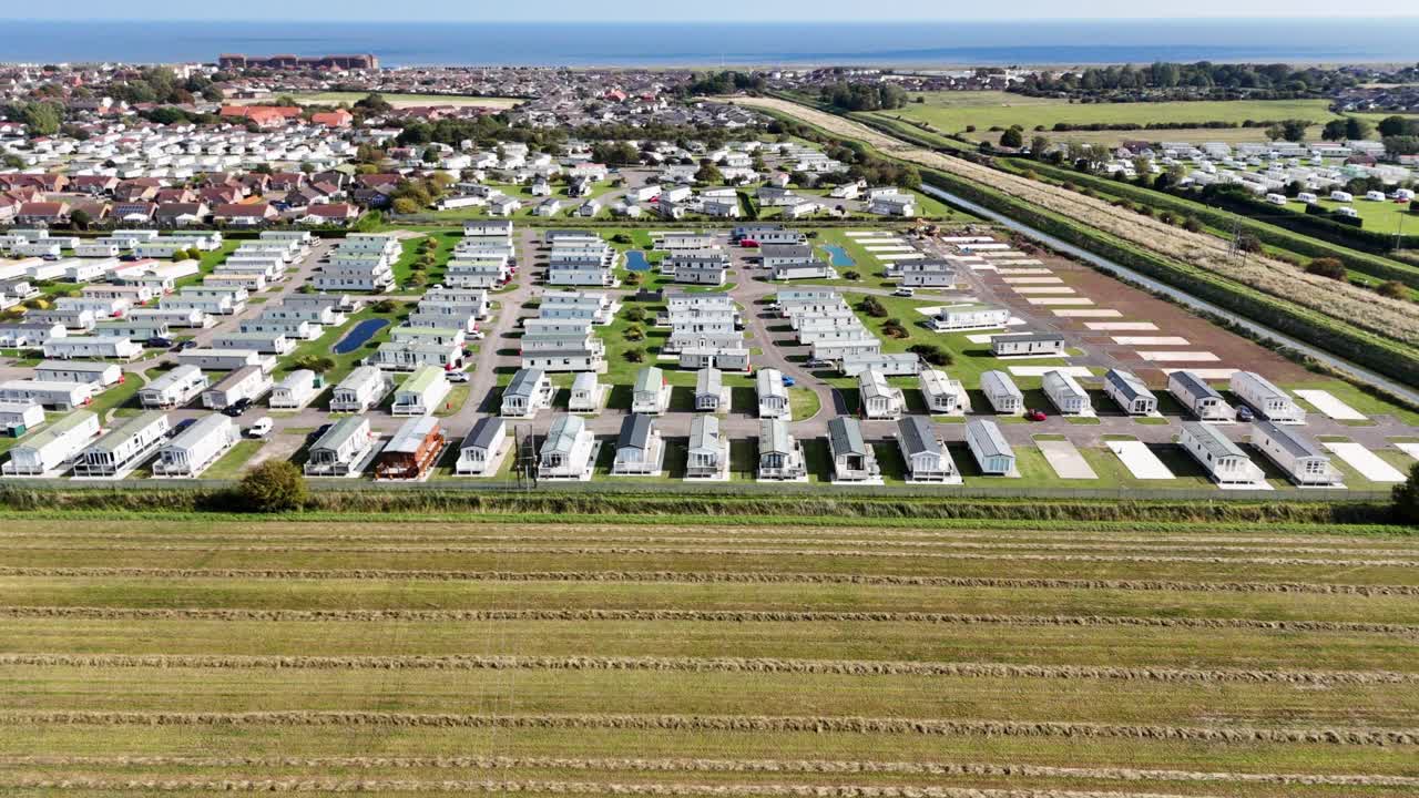 Rotating aerial view of a static caravan trailer park next to the beach with all the caravans holiday homes set out in neat rows