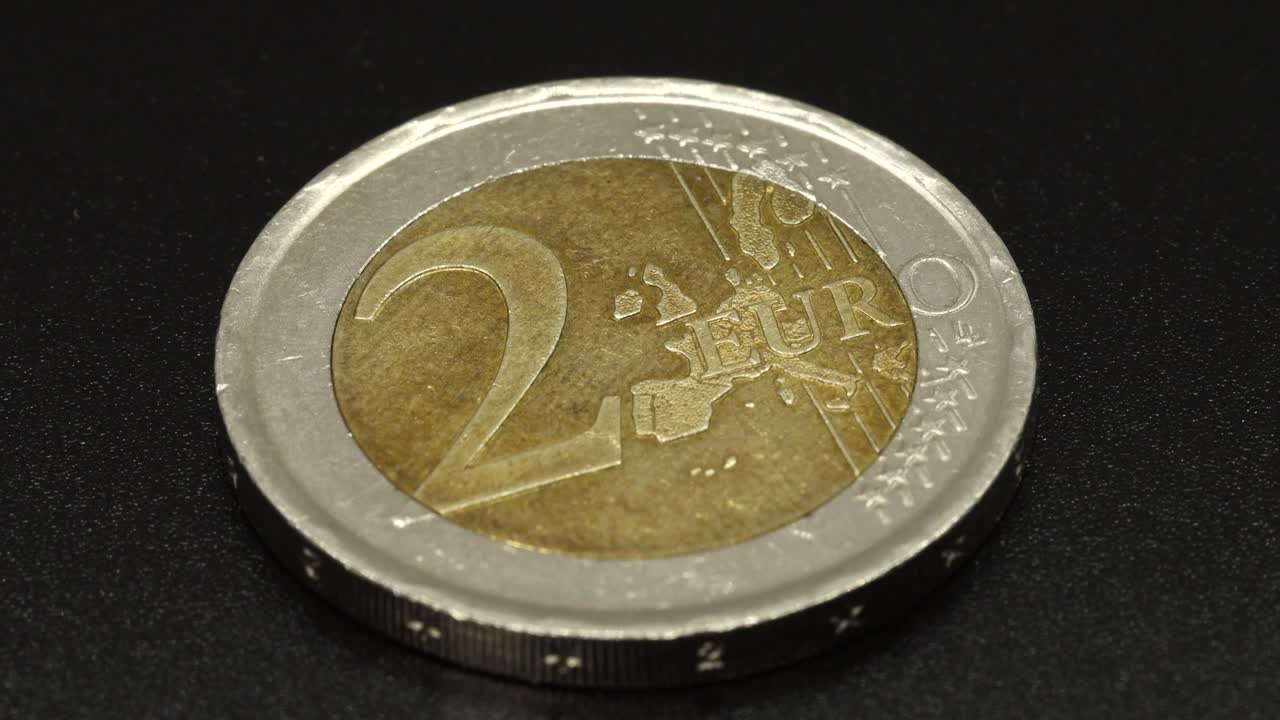 una brillante moneda de dos euros girando sobre fondo de superficie negra en 4k