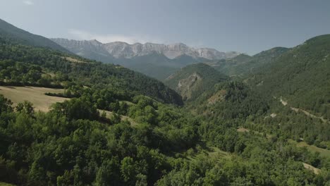 aerial view of a drone advancing in between mountains and above the forest, with the mountain range of cadi on the horizon