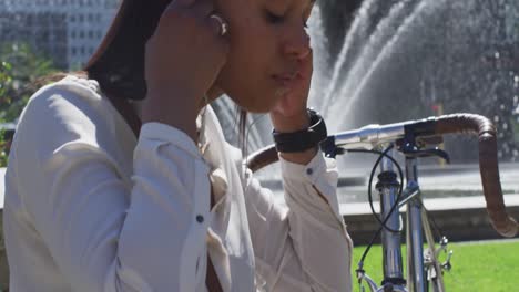 african american woman with bike putting earphones on in city park