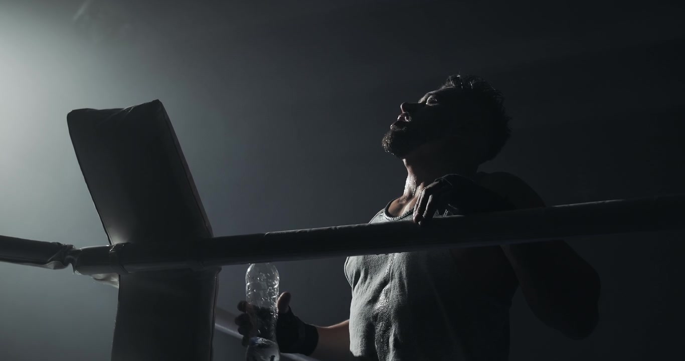 Pugile stanco che beve acqua e si rinfresca in un ring buio.