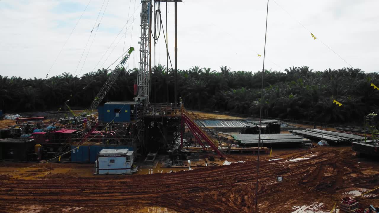 imágenes cinematográficas de drones de 4k de la estructura del equipo de la plataforma de perforación en tierra para la exploración y explotación de petróleo en medio de la jungla rodeada de palmeras durante la puesta de sol y el alto precio del petróleo
