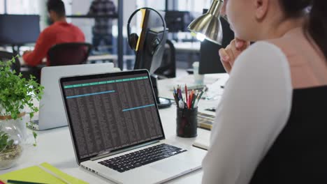 caucasian woman sitting at desk watching coding data processing on laptop screen