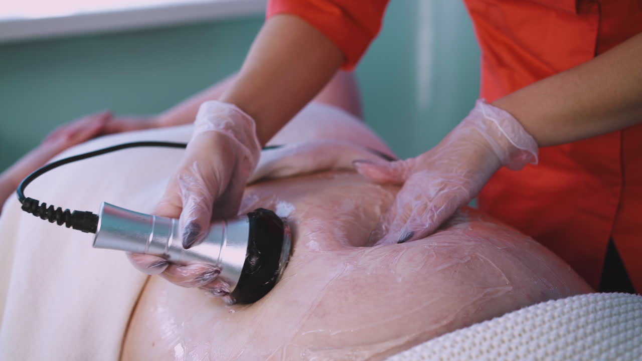 косметолог проводит процедуру вибромассажа для большой женщины