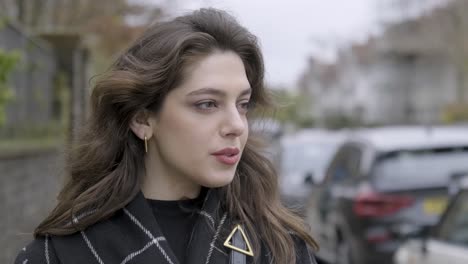 portrait of a brunette woman looking at city life standing in the middle of modern urban city street, wearing spring coat