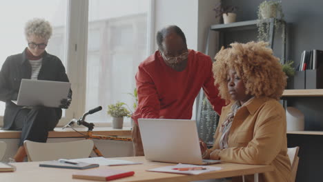 black man and woman speaking and using laptop in office