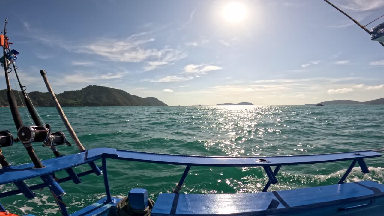 A fishing boat navigates Phuket's turquoise waters under bright sunlight, showcasing fishing rods and scenic island views