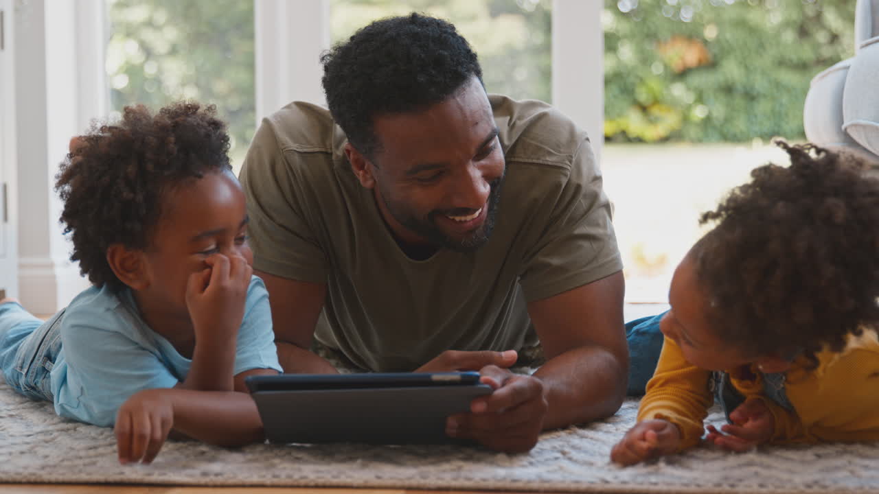 Padre a casa con i bambini sdraiati sul tappeto che giocano con un tablet digitale