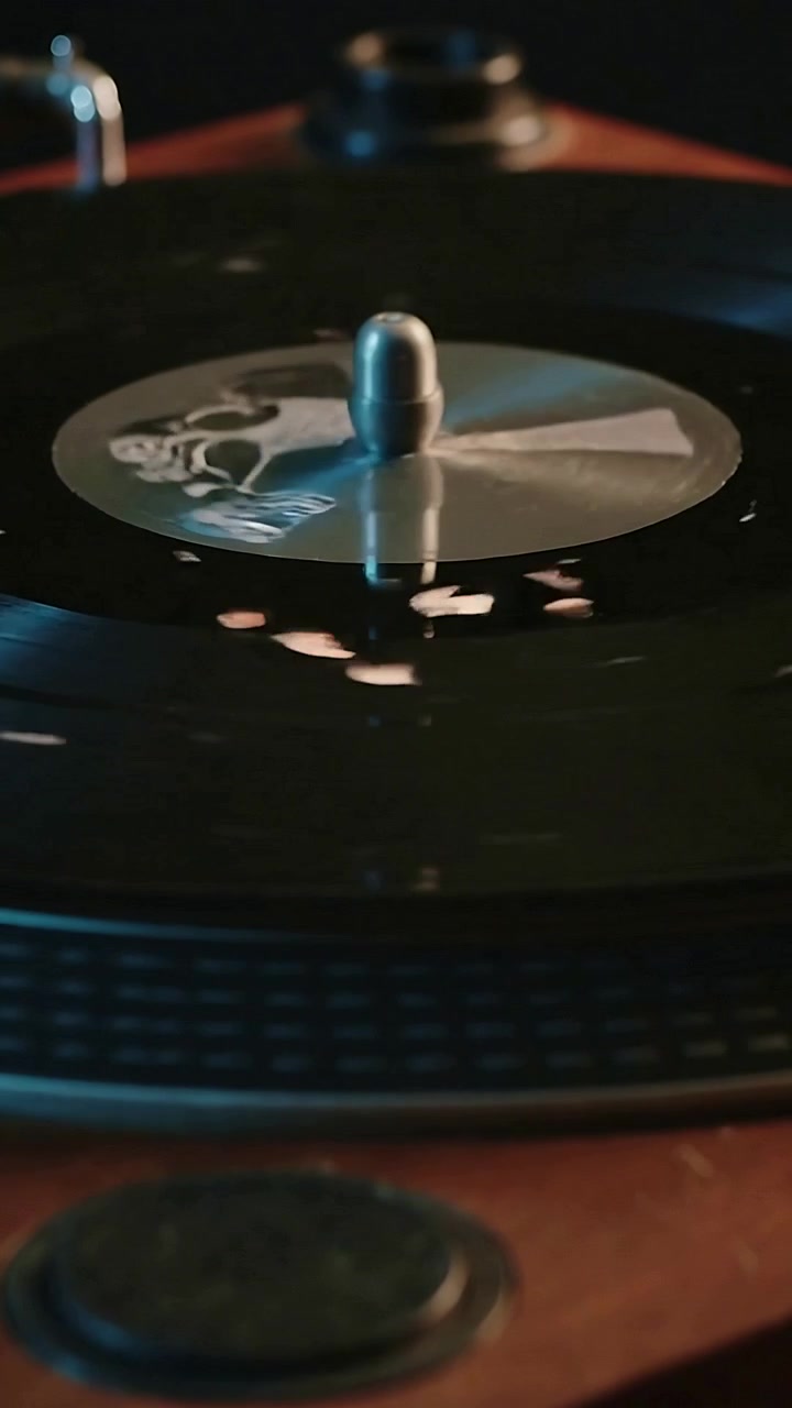 Video verticale: Vinile che gira con il perno sul giradischi dopo l'avvio del motore per riprodurre musica, luci calde.