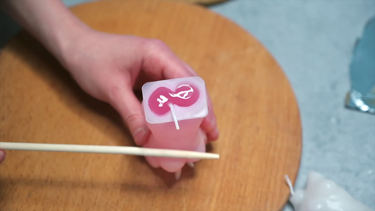 A woman occupied with hand made candles production, tapping the mold with melted wax with a stick. Slow motion