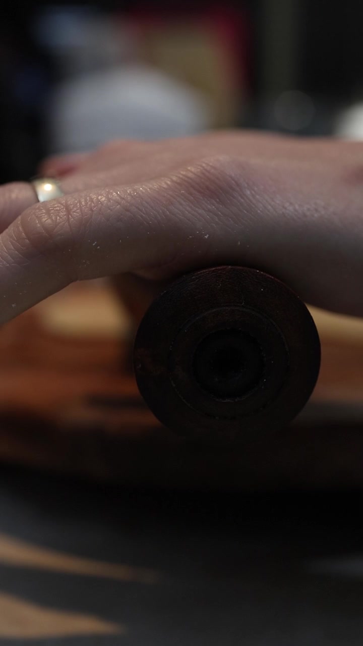 Primo piano di mani delicate che stendono l'impasto del chapati su una superficie di legno con un mattarello, scena di cucina intima con illuminazione calda e sfondo sfocato